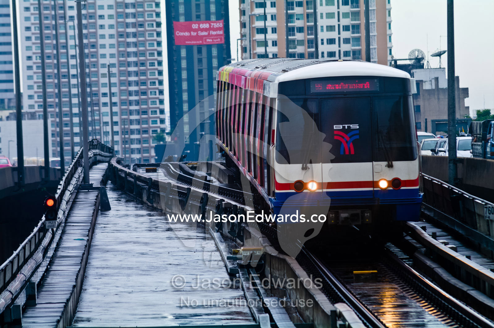 A commuter train approaches a station platform on a rainy day. Bangkok, Thailand.