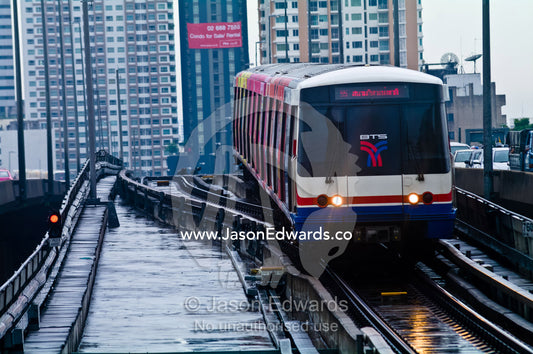 A commuter train approaches a station platform on a rainy day. Bangkok, Thailand.