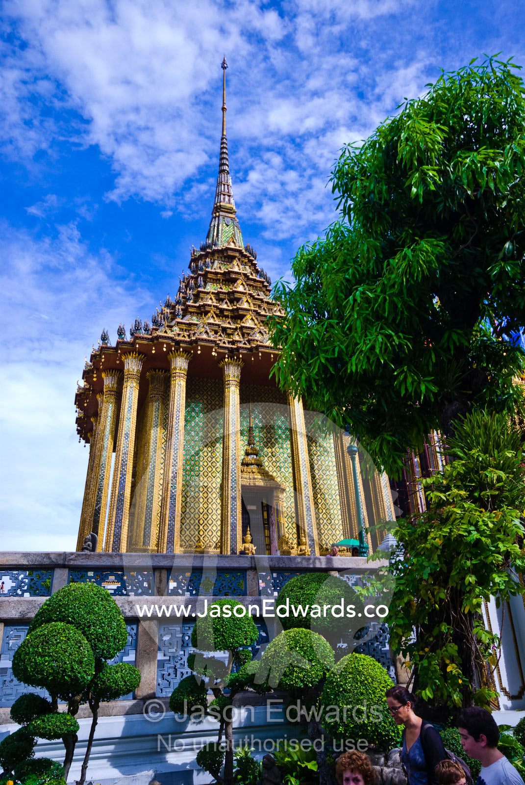 Sculptured gardens surround a gilded Buddhist temple and spire. Prasat Phra Thep Bidon, Royal Pantheon, Wat Phra Kaew, Wat Phra Kaeo, Temple of the Emerald Buddha, Bangkok, Thailand.