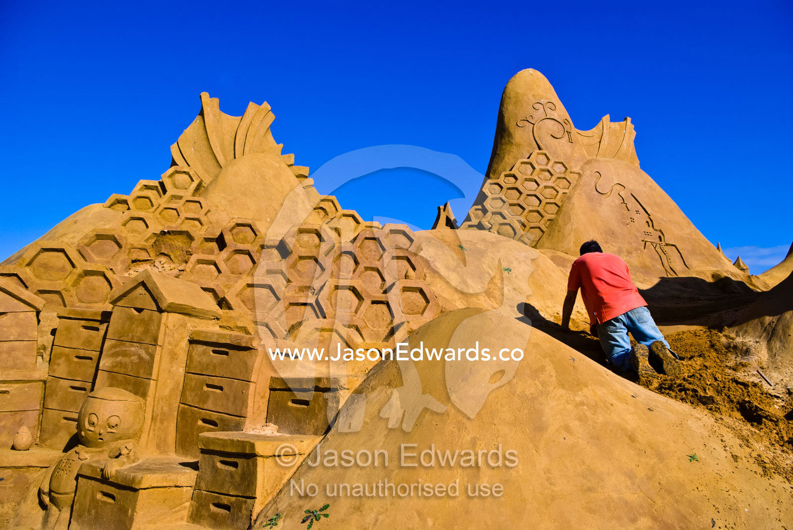 A professional sand sculptor carves a bee hive honeycomb sculpture. Frankston, Port Phillip Bay, Melbourne, Victoria, Australia.