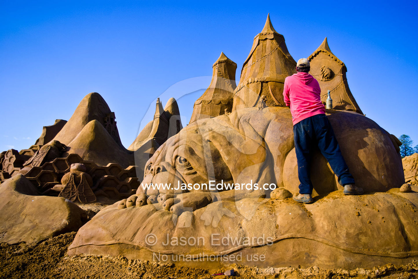 A professional sand sculptor carves a sculpture of a droopy eyed dog. Frankston, Port Phillip Bay, Melbourne, Victoria, Australia.