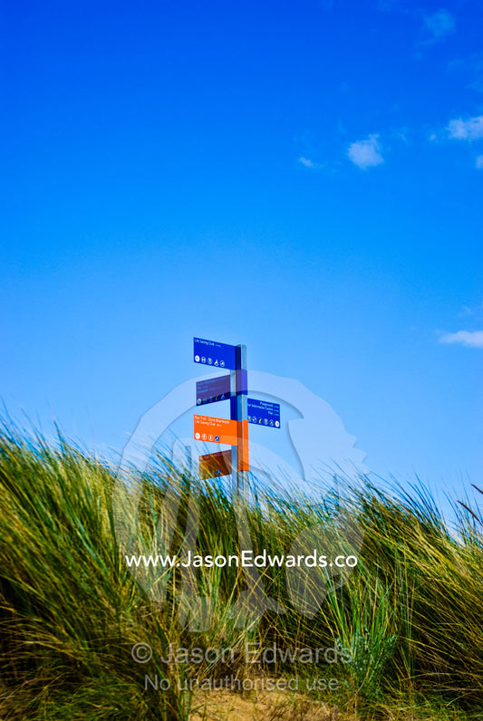 A colourful street sign atop a sand dune for beachside walking trails. Frankston, Port Phillip Bay, Melbourne, Victoria, Australia.