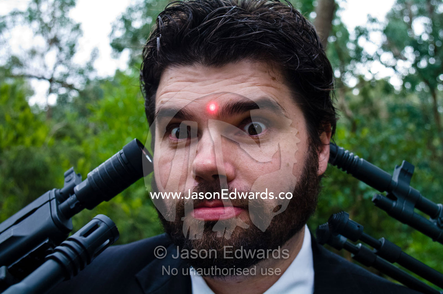 Groomsmen point gun barrels at the head of a groom on his wedding day. Park Orchards, Melbourne, Victoria, Australia.