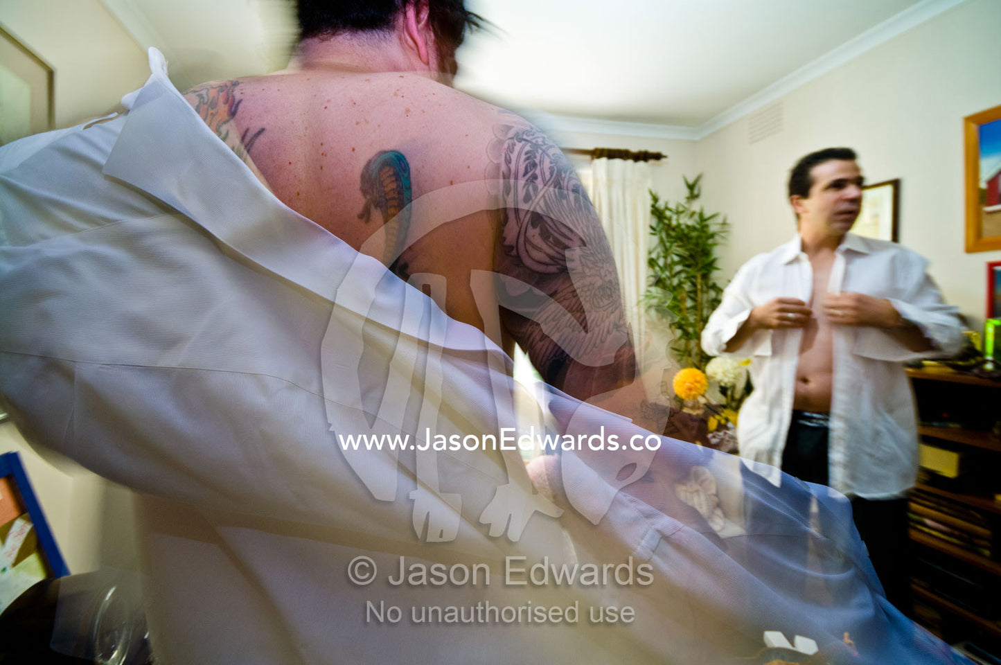 A tattooed groomsmen getting dressed in shirt and suit for a wedding. Park Orchards, Melbourne, Victoria, Australia.