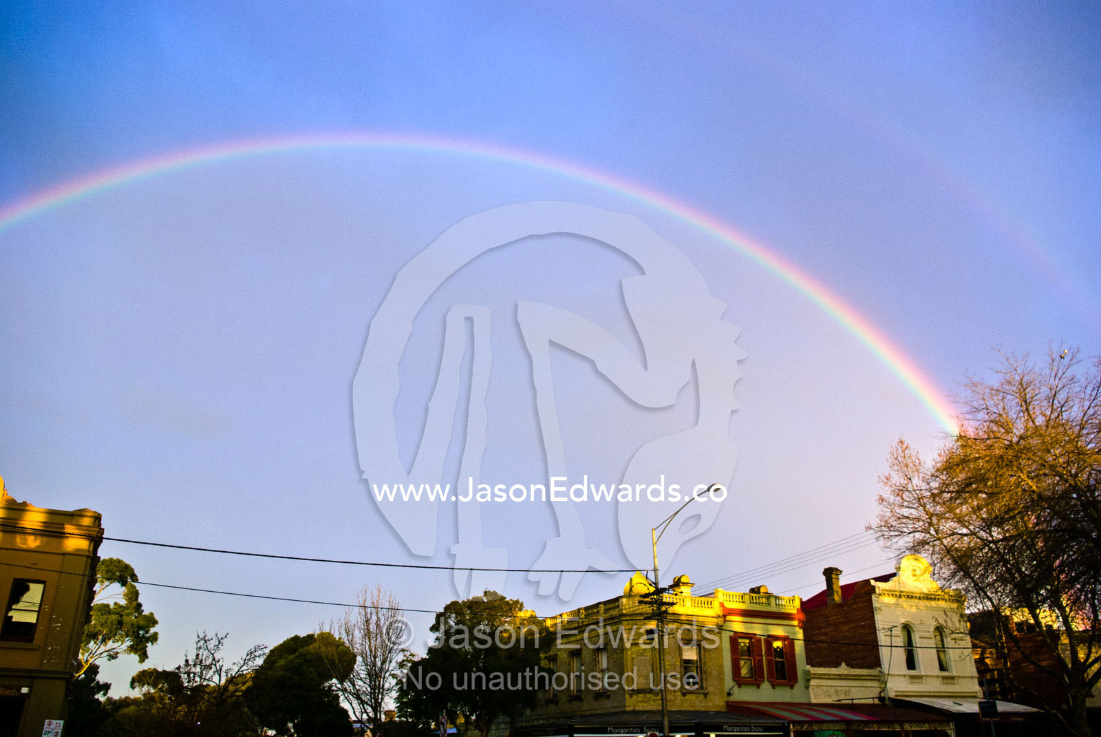 An  iridescent rainbow arches over a row of heritage shop facades. North Carlton, Melbourne, Victoria, Australia.