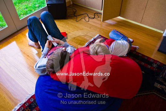 Two boys resting on colourful bean bags watching television. Malvern East, Melbourne, Victoria, Australia.
