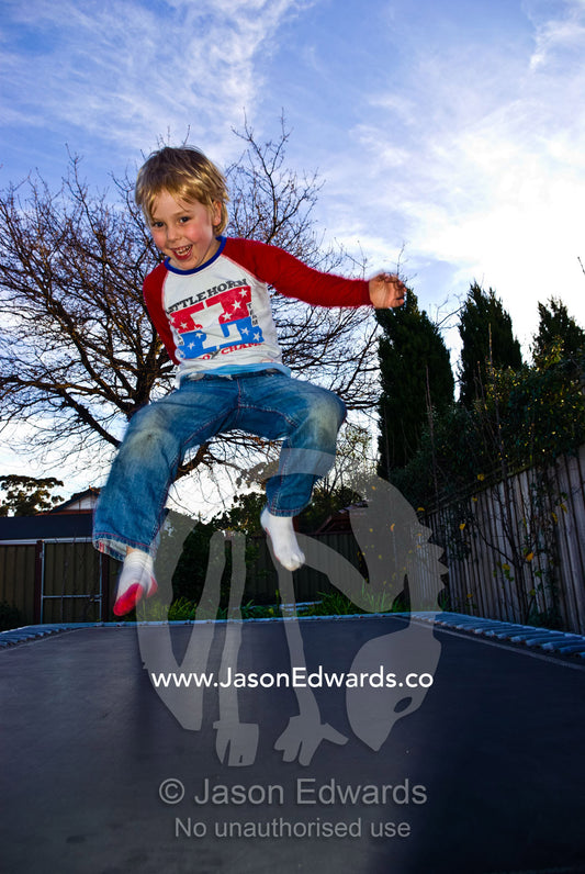 A boy laughs as he bounces for joy on a suburban backyard trampoline. Malvern East, Melbourne, Victoria, Australia.
