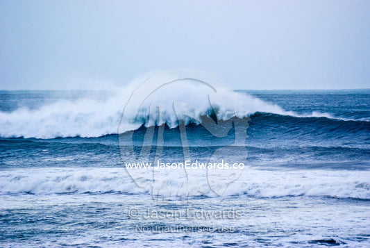 Huge foaming surf rolls in over a reef break during a winter swell. Point Danger, Torquay, Surf Coast, Victoria, Australia.
