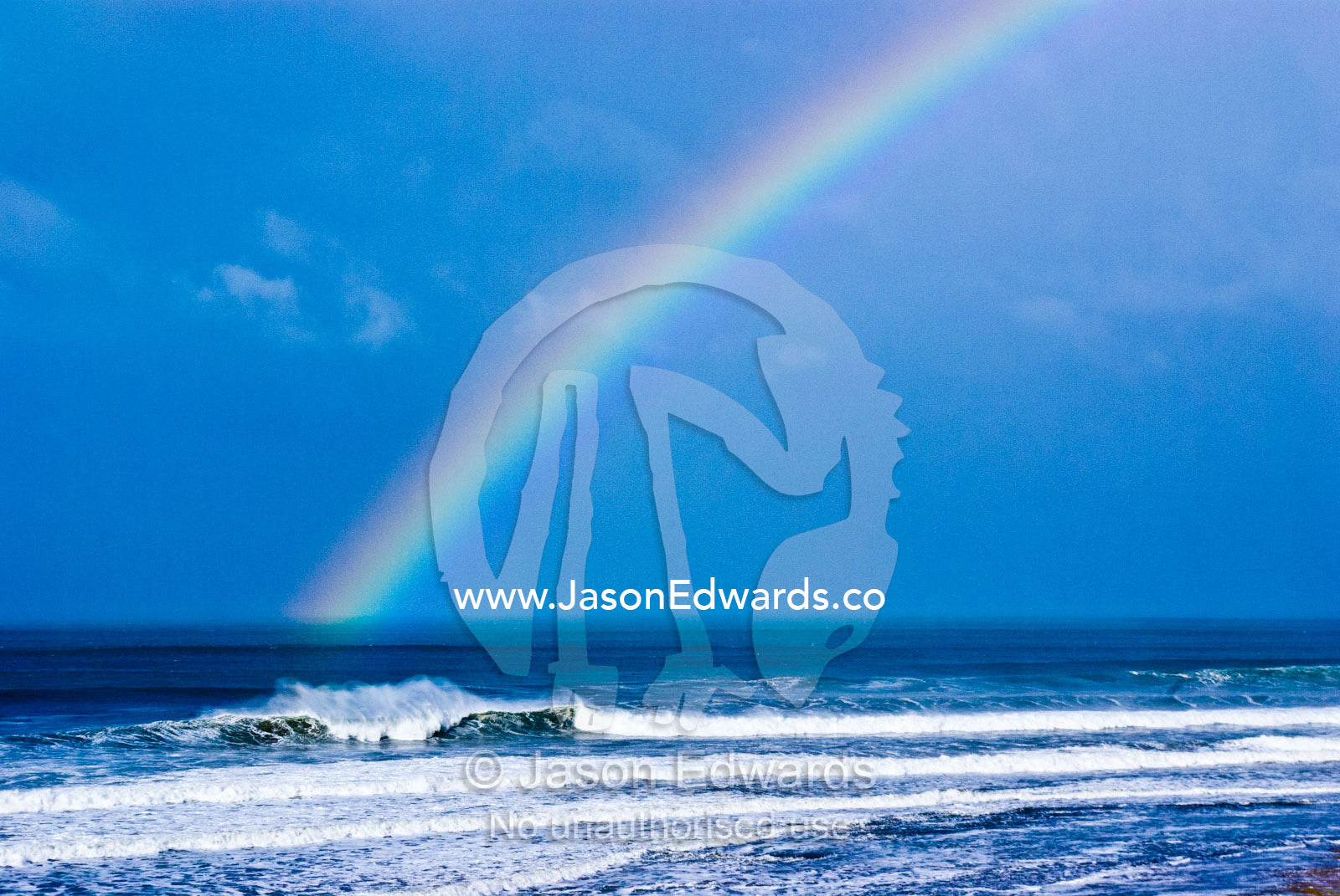 An iridescent rainbow touches the ocean and huge waves at Bells Beach. Bells Beach Surfing Recreation Reserve, Surf Coast, Victoria, Australia.