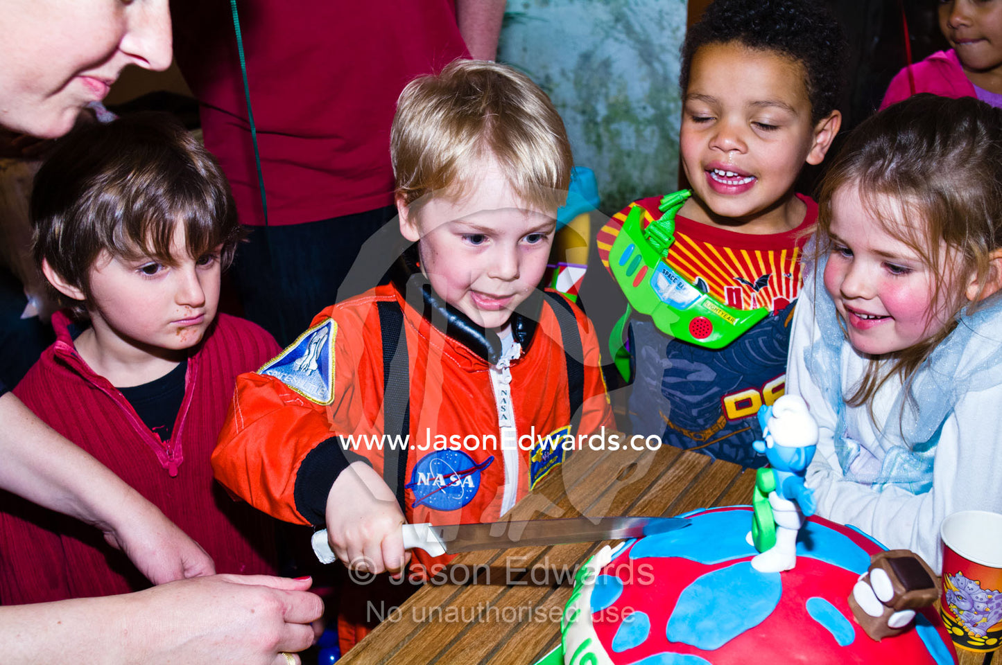 Supervised  by his mum a boy cuts his birthday cake with friends. North Carlton, Melbourne, Victoria, Australia.
