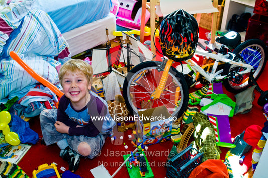 A smiling boy in his messy bedroom surrounded by his toys and bike. North Carlton, Melbourne, Victoria, Australia.