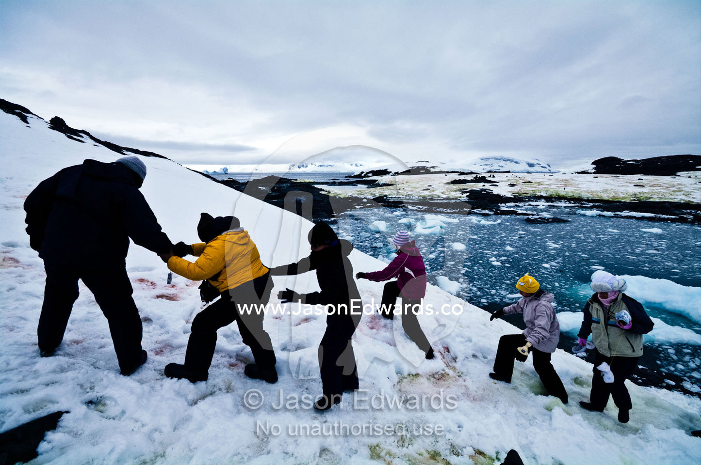 Tourists help each other clamber up a snowy slope in Antarctica. Station W, Detaille Island, Antarctic Peninsula, Antarctic Circle, Antarctica.