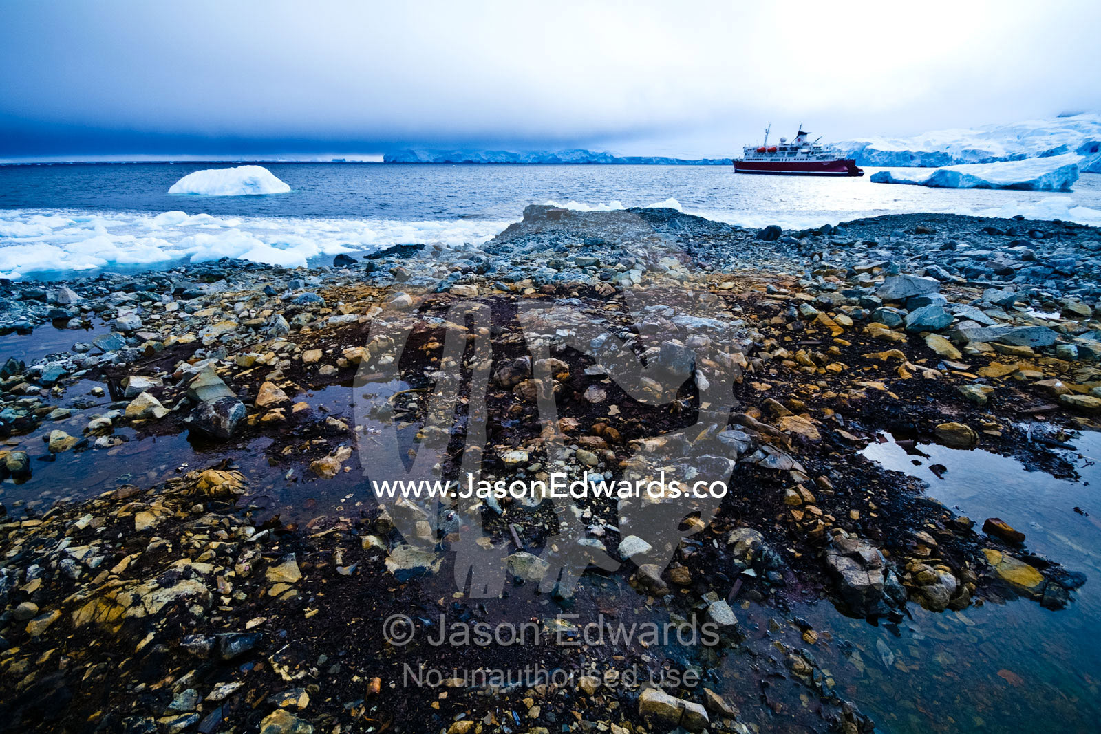 An Antarctic cruise ship anchored in an icy bay off a rocky shore. Prospect Point, Crystal Sound, Antarctic Peninsula, Antarctic Circle, Antarctica.