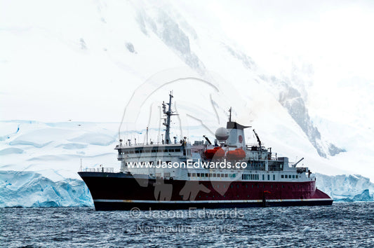 An Antarctic cruise ship anchored by a snow and ice encrusted peak. Crystal Sound, Hanusse Bay, Antarctic Peninsula, Antarctic Circle, Antarctica.