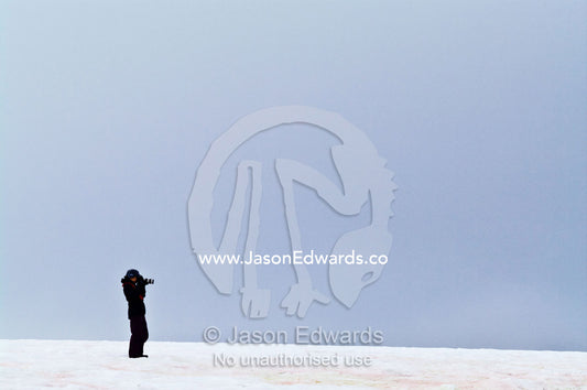 A lone tourist photographing on a windswept hillside in Antarctica. Prospect Point, Crystal Sound, Antarctic Peninsula, Antarctic Circle, Antarctica.