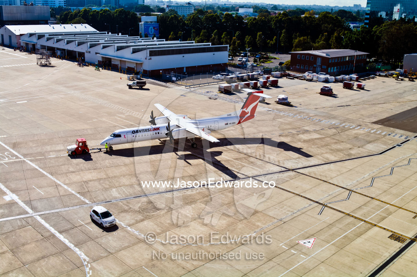 A tractor known as an airplane tug tows a plane across the tarmac. Kingsford Smith Airport, Mascot, Sydney, New South Wales, Australia.
