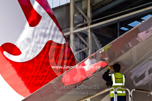 An aeronautical engineer repairs a jet airliner wing from a crane. Kingsford Smith Airport, Mascot, Sydney, New South Wales, Australia.