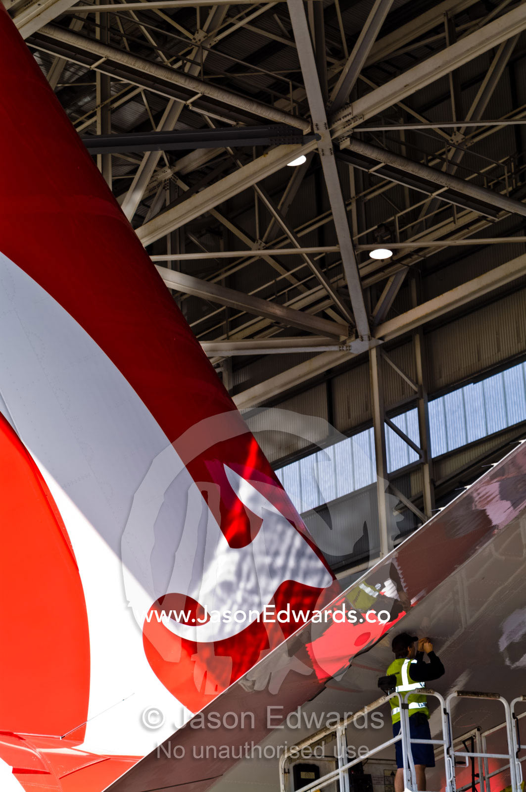 An aeronautical engineer repairs a jet airliner wing from a crane. Kingsford Smith Airport, Mascot, Sydney, New South Wales, Australia.