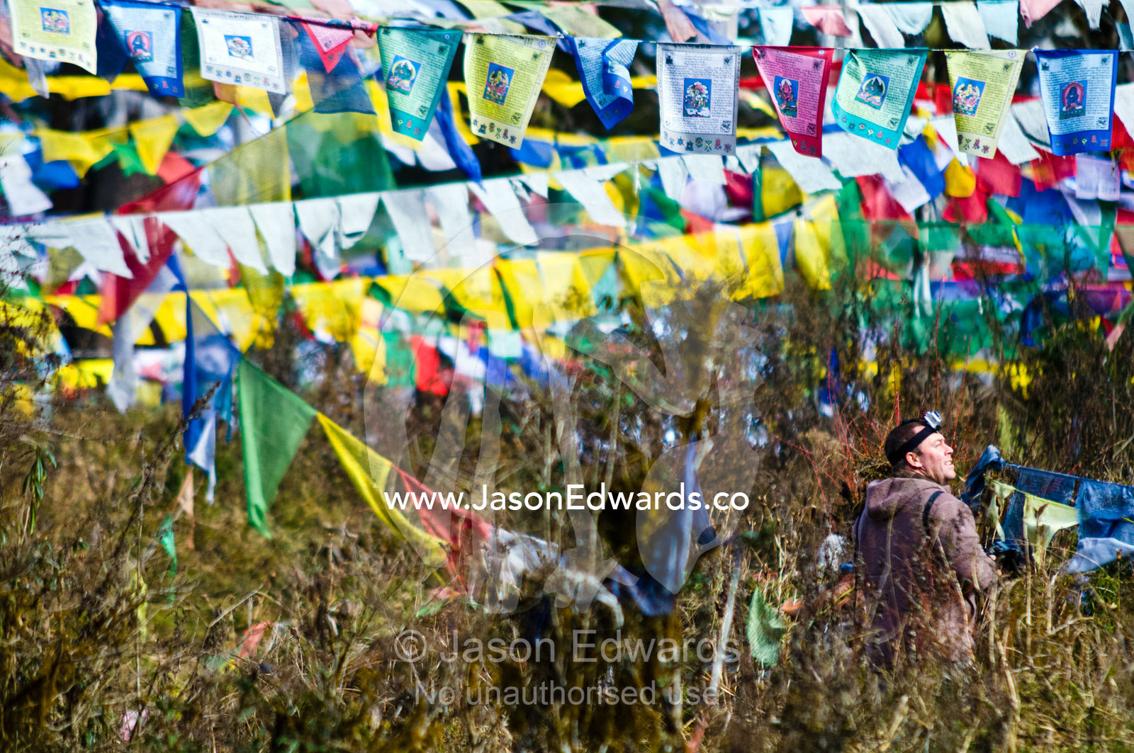 A photographer walks among a canopy of prayer flags on a mountainside. 108 Druk Wangyal Khangzang Chortens, Dochula Pass, Thimphu District, Bhutan.