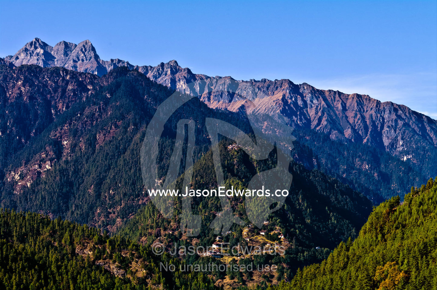 A rugged Himalayan mountain ridge above a small village in a dense forest. Jigme Dorji National Park, Gasa District, Bhutan.