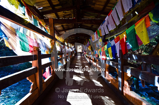 Prayer flags adorn a covered bridge that crosses a river to a monastery. Cheri Monastery, Chagri Dorjeden Monastery, Thimphu, Thimphu District, Bhutan.
