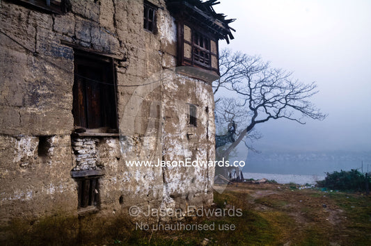 A weathered and rustic Bhutanese home on the shore of a river shrouded in mist. Punakha River, Punakha Valley, Punakha-Wangdiphodrang District, Bhutan.
