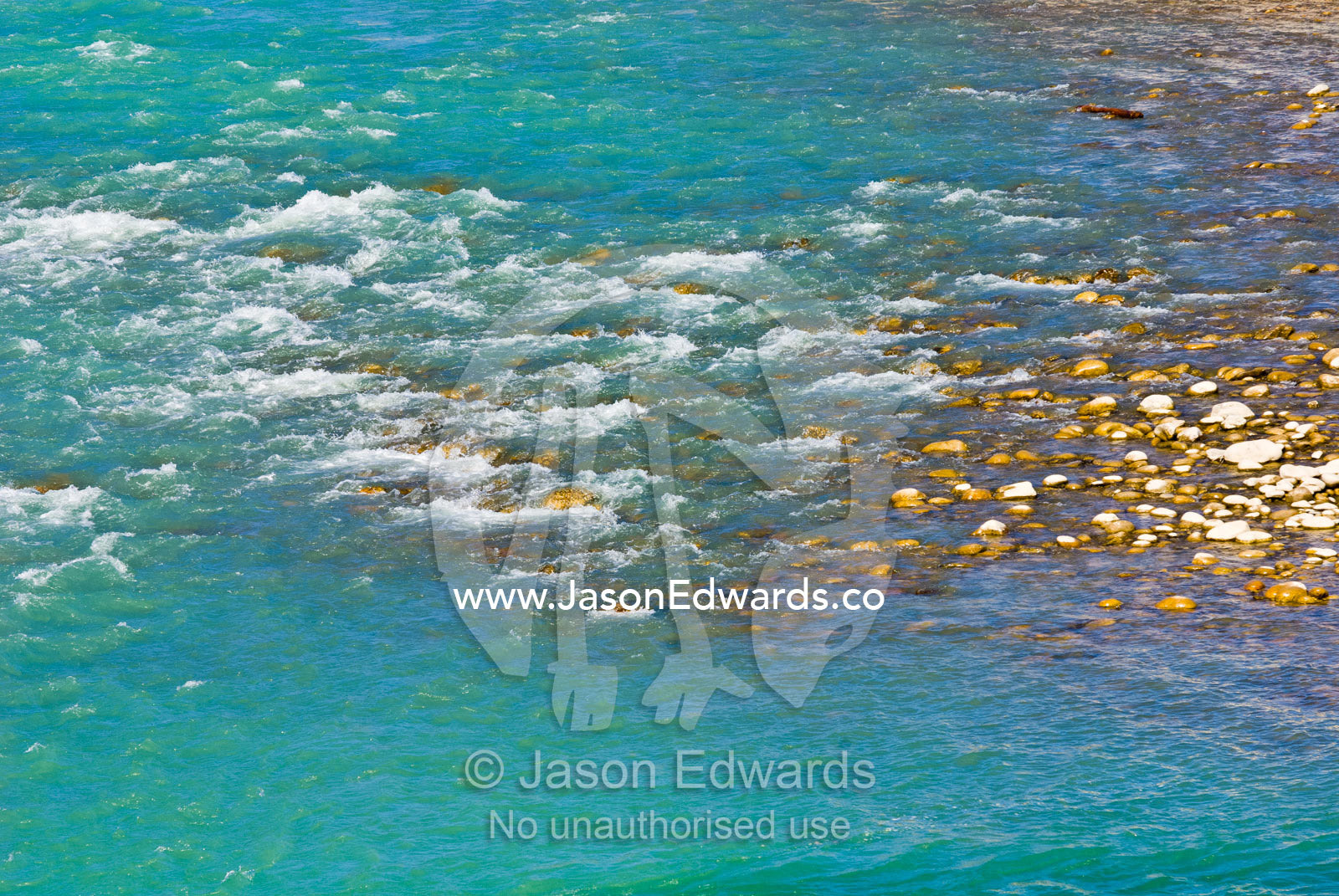 Turquoise rapids from an alpine river flow over river stones next to a Buddhist monastery. Punakha Dzong, Punakha dzongkhag, Punakha District, Bhutan.