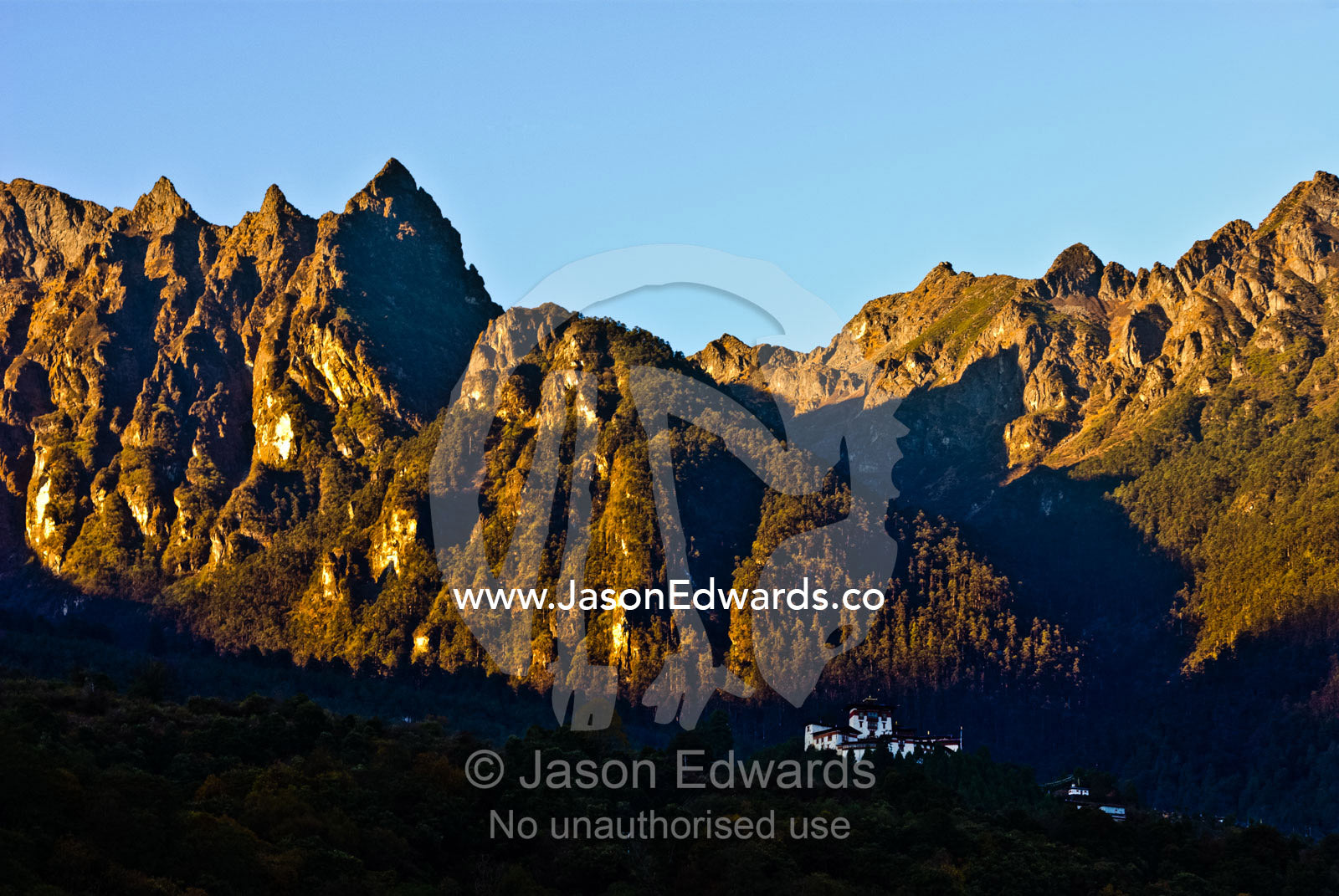 A Buddhist monastery falls into the shadow of a jagged mountain valley at sunset. Gasa Dzong, Gasa Tashi Tongmon Dzong, Gasa Gasa Dzongkhag District, Bhutan.