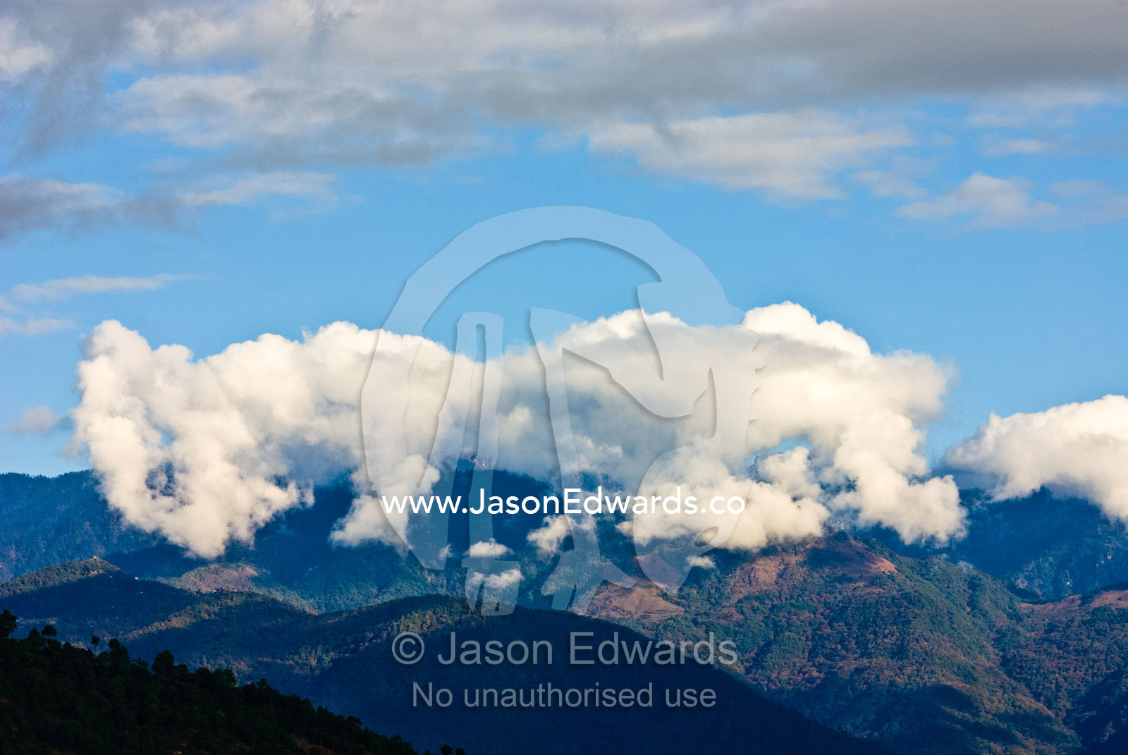 Clouds cap a forested mountain range in the Himalaya. 108 Druk Wangyal Khangzang Chortens, Dochula Pass, Thimphu District, Bhutan.