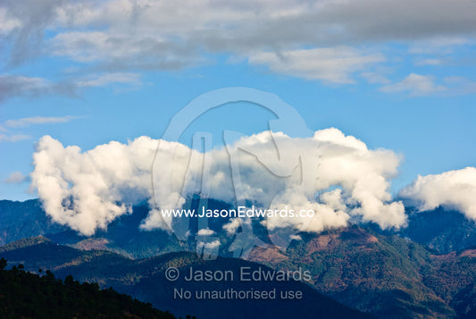Clouds cap a forested mountain range in the Himalaya. 108 Druk Wangyal Khangzang Chortens, Dochula Pass, Thimphu District, Bhutan.
