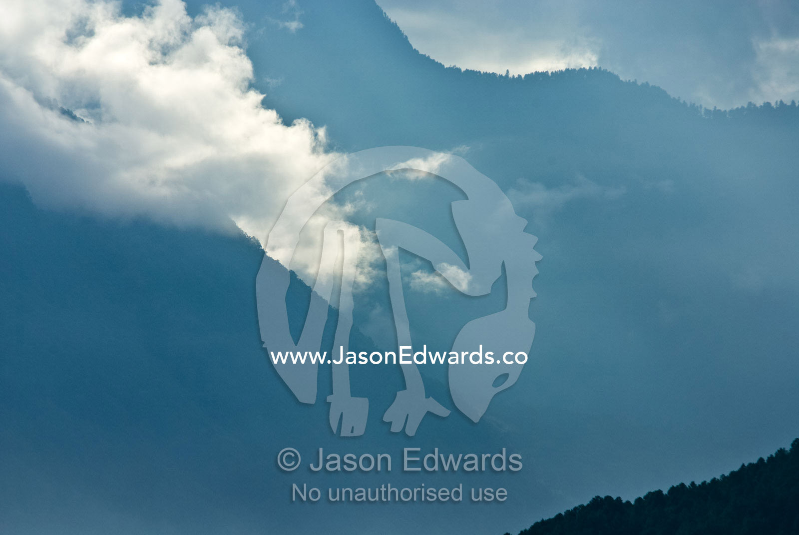 Backlit clouds and mist descend into a steep mountain valley shrouded in dense forest. Jigme Dorji National Park, Gasa District, Bhutan.
