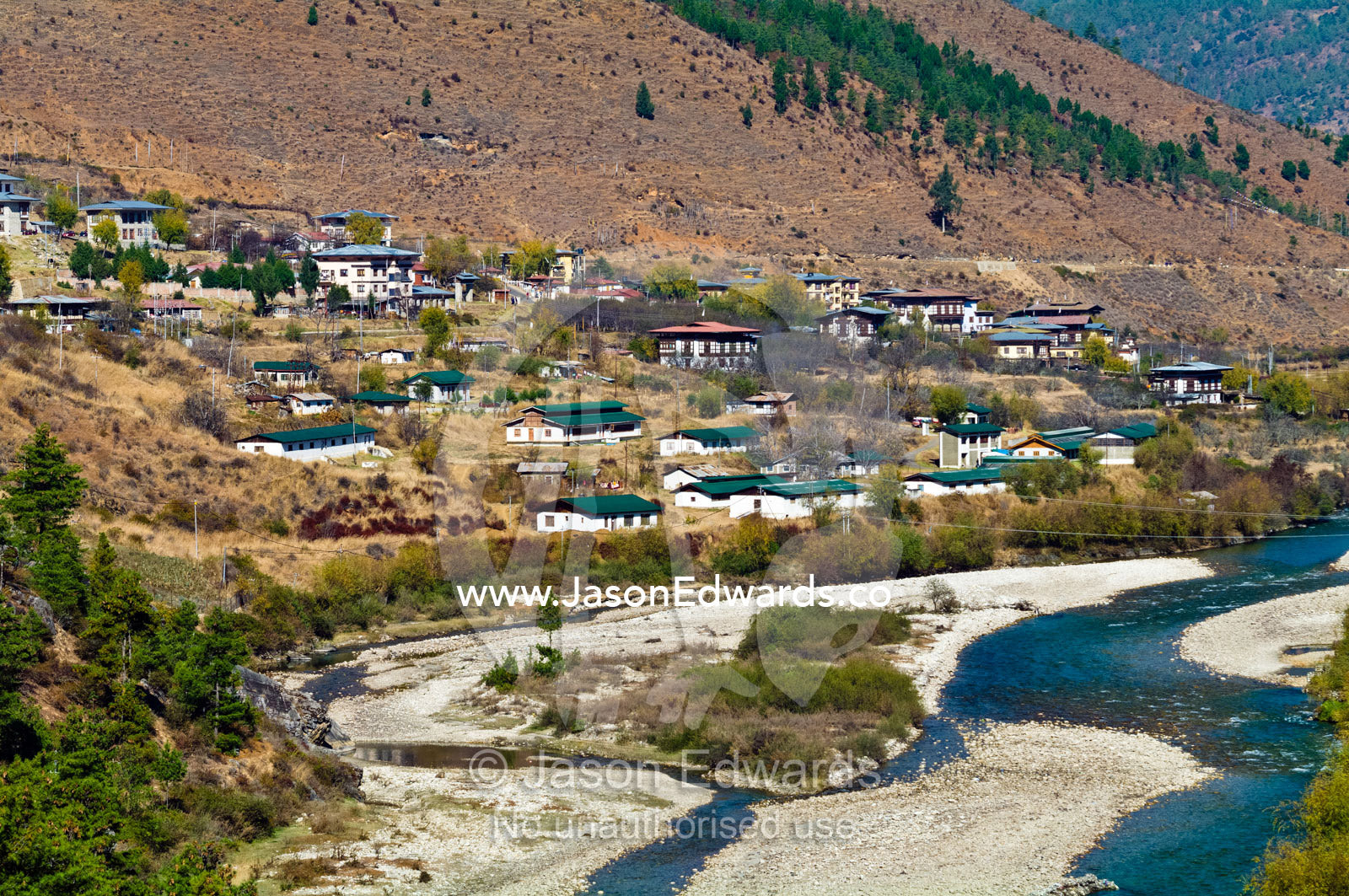 The turquoise waters of the alpine Paro River meander the a town nestled on a barren hillside. Paro River, Paro Chu, Paro, Paro District, Bhutan.