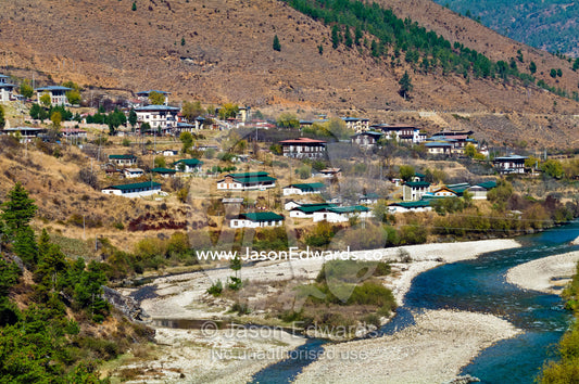 The turquoise waters of the alpine Paro River meander the a town nestled on a barren hillside. Paro River, Paro Chu, Paro, Paro District, Bhutan.
