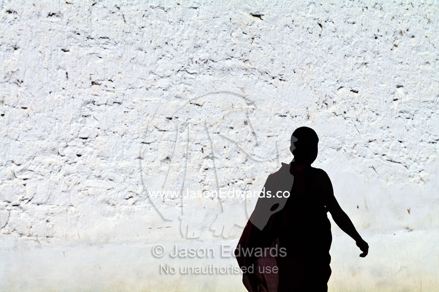 A Buddhist monk strolls past a white-washed wall in his robes on the way to prayers. Rinpung Dzong, Paro Dzong, Paro, Paro District, Bhutan.