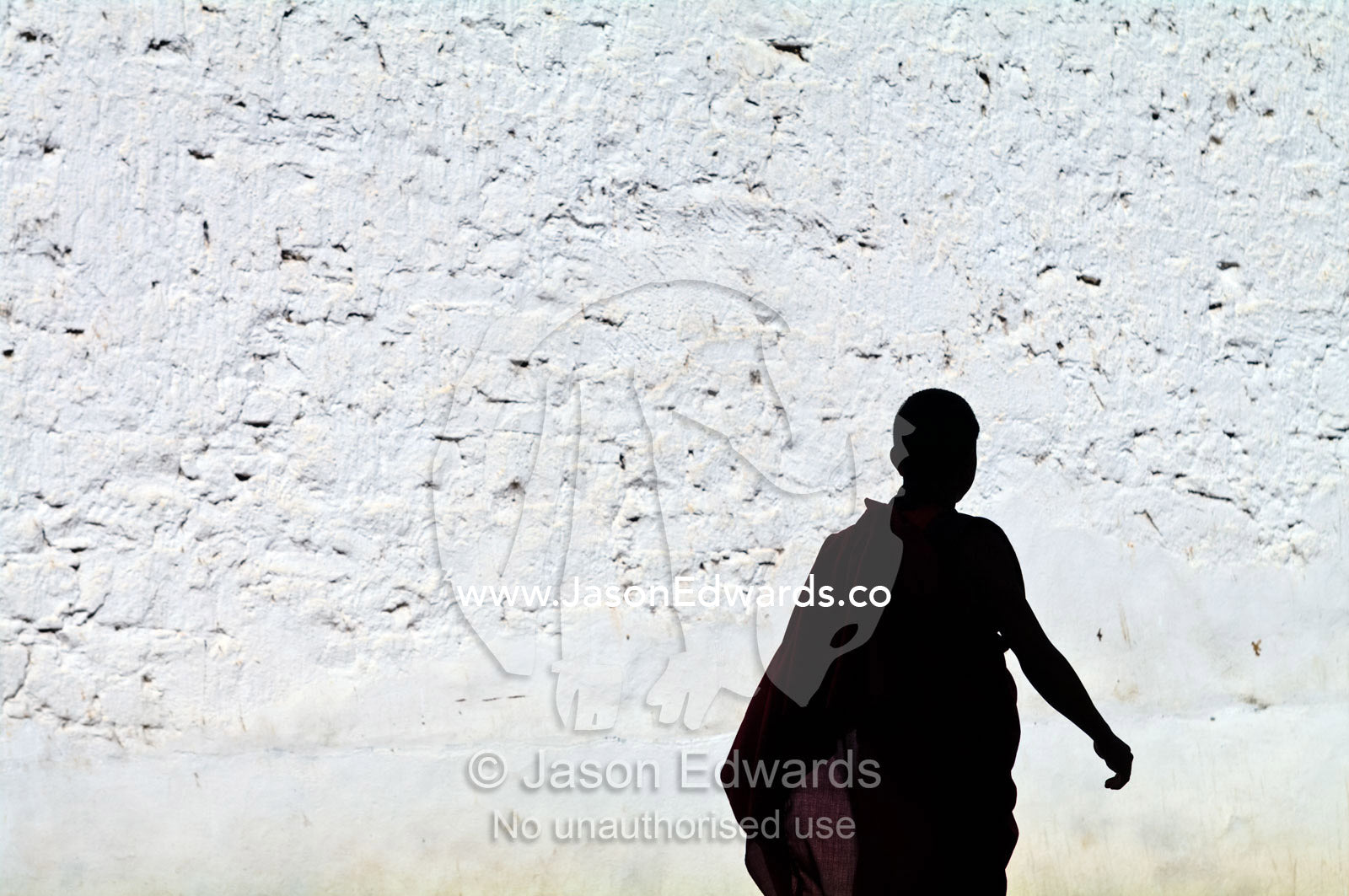 A Buddhist monk strolls past a white-washed wall in his robes on the way to prayers. Rinpung Dzong, Paro Dzong, Paro, Paro District, Bhutan.