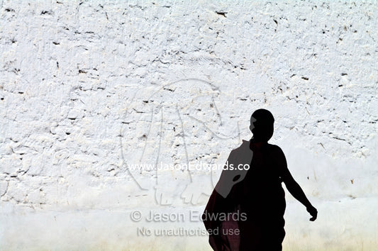 A Buddhist monk strolls past a white-washed wall in his robes on the way to prayers. Rinpung Dzong, Paro Dzong, Paro, Paro District, Bhutan.
