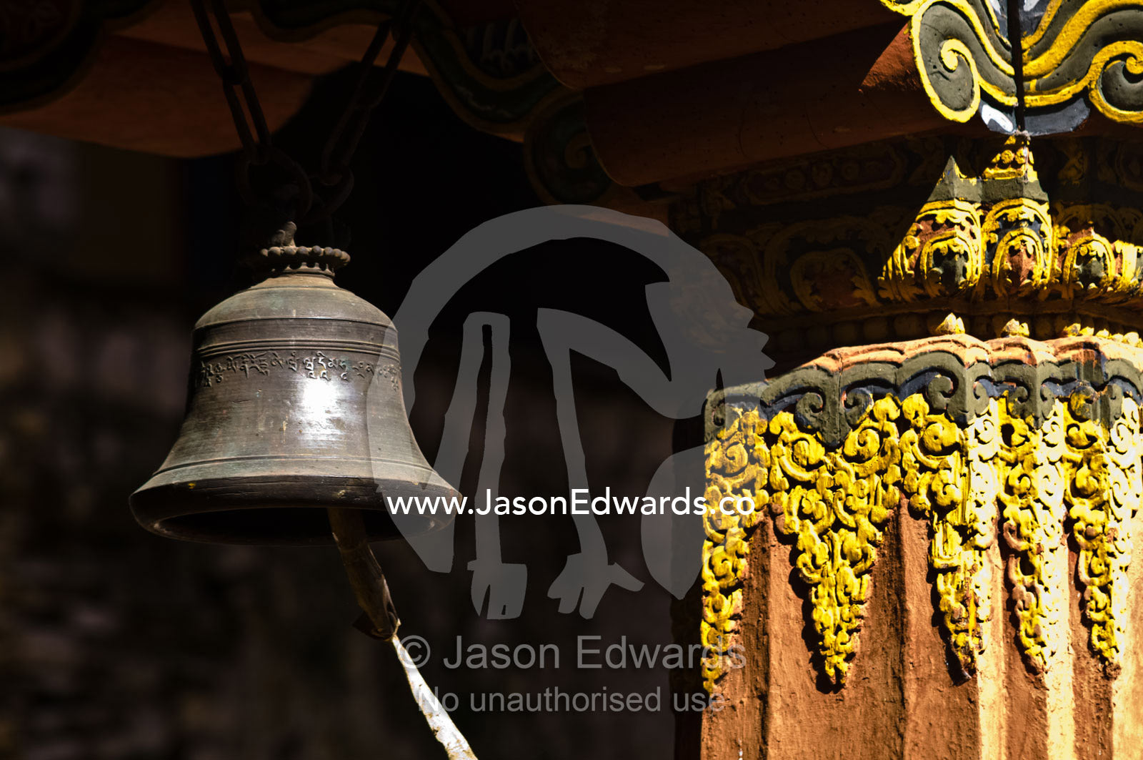 A brass meditation bell hangs from an ornate eve in a Buddhist monastery. Rinpung Dzong, Paro Dzong, Paro, Paro District, Bhutan.