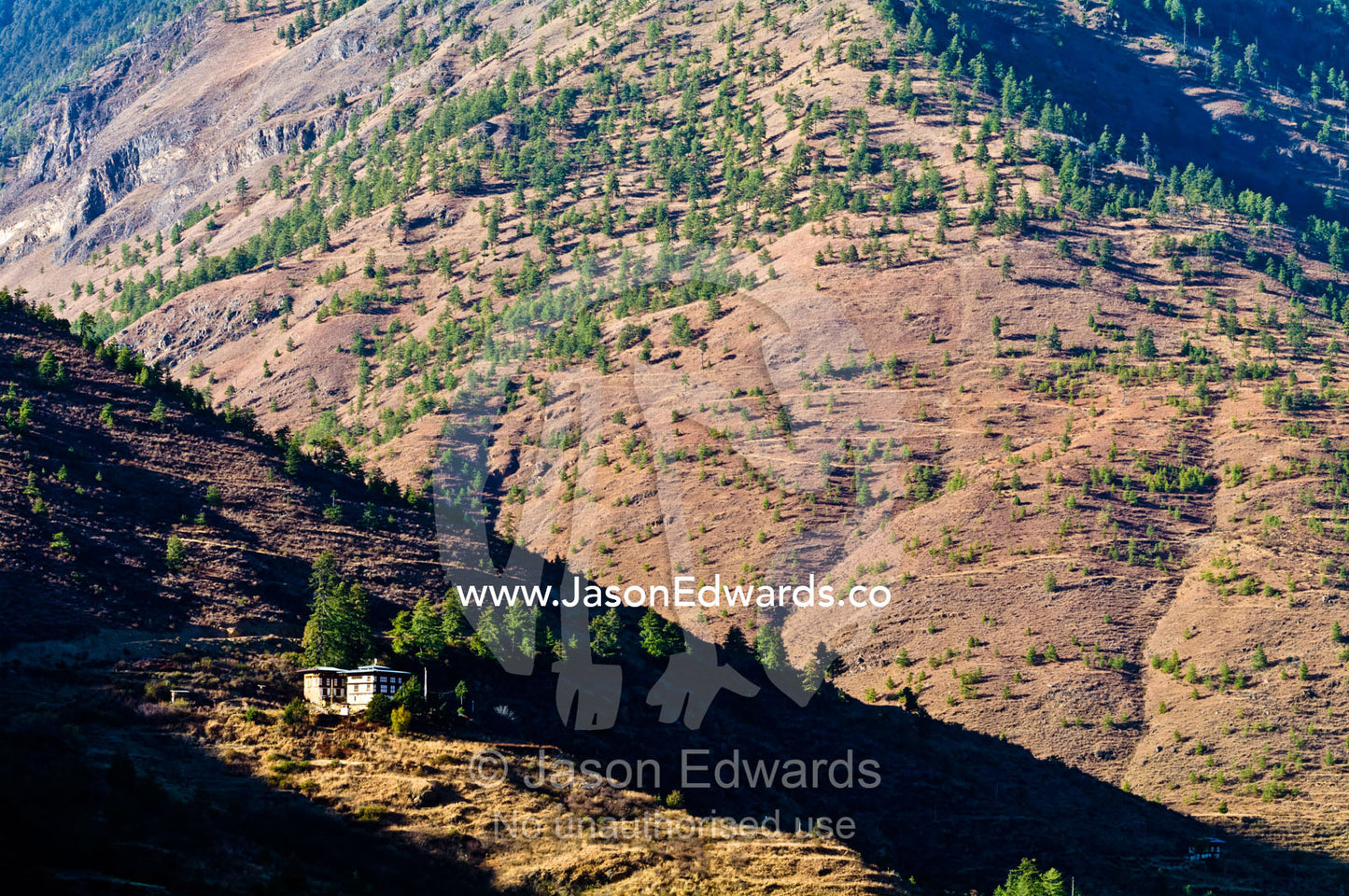 A traditional Bhutanese farmhouse on a rugged mountainside catches the last rays of the setting sun. Thimphu District, Bhutan.