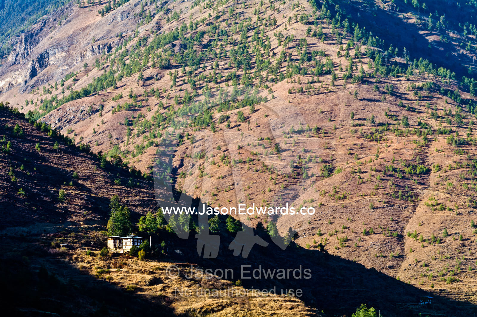 A traditional Bhutanese farmhouse on a rugged mountainside catches the last rays of the setting sun. Thimphu District, Bhutan.