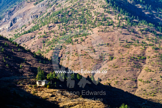 A traditional Bhutanese farmhouse on a rugged mountainside catches the last rays of the setting sun. Thimphu District, Bhutan.