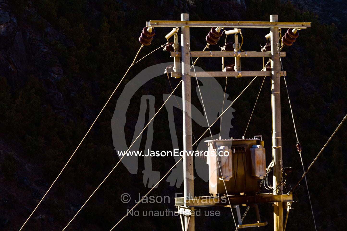 Electricity pole, cables and transformer catch the sunset as a mountain valley falls into shadow. Thimphu District, Bhutan.