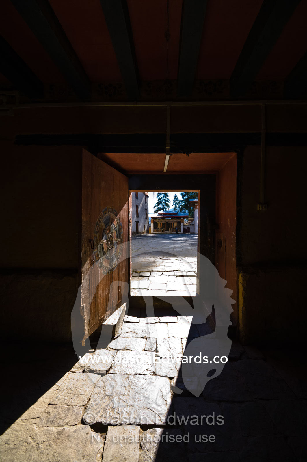 Sunlight shining through an ancient wooden door onto the stone paved floor of an astrology school. Pangri Zampa Astrology School, Thimphu, Thimphu District, Bhutan.