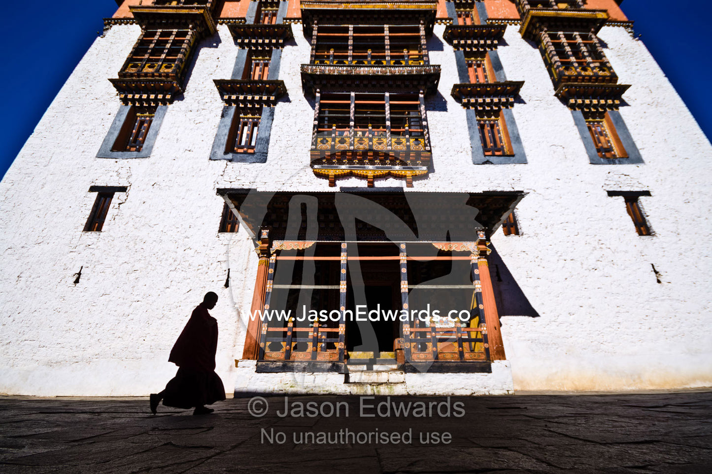 A Buddhist monk runs through an ancient monastery courtyard running late for prayers. Rinpung Dzong, Paro Dzong, Paro, Paro District, Bhutan.
