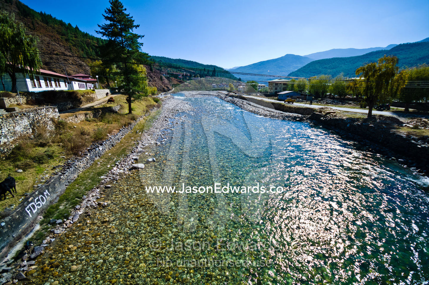 The clear turquoise alpine waters of the Paro River travel past a Buddhist monastery. Paro Chu, Paro River, Rinpung Dzong, Paro Dzong, Paro, Paro District, Bhutan.