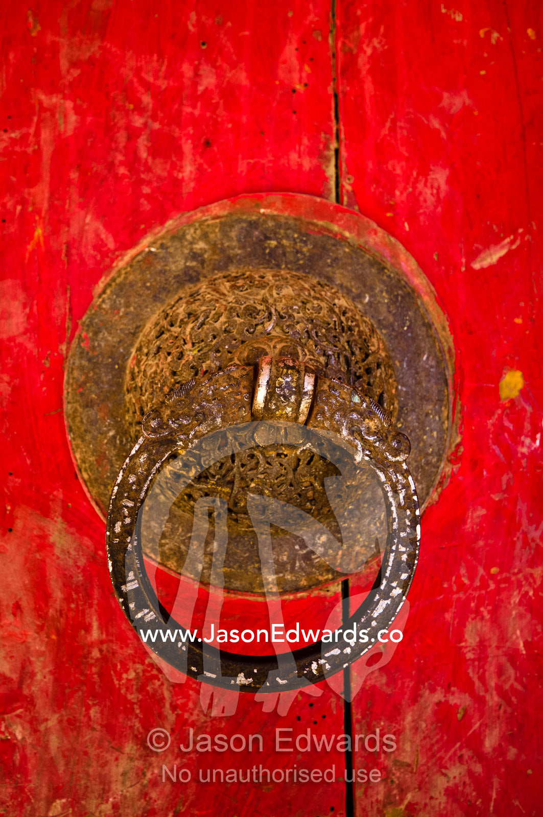 A rusting door knocker on a weathered bright red door leading to a Buddhist monastery. Gangteng Monastery, Ganteng, Wangdue Phodrang District, Phobjika Valley, Phobjikha Valley, Gangteng Valley, Black Mountains, Bhutan.