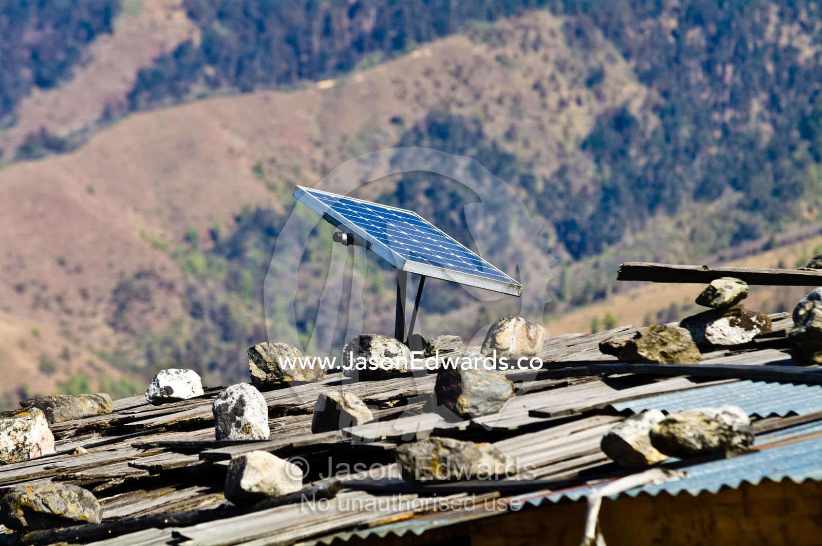 A solar panel generates electricity for a village home with a corrugated tin roof held in place by rocks. Ganteng, Wangdue Phodrang District, Phobjika Valley, Phobjikha Valley, Gangteng Valley, Black Mountains, Bhutan.