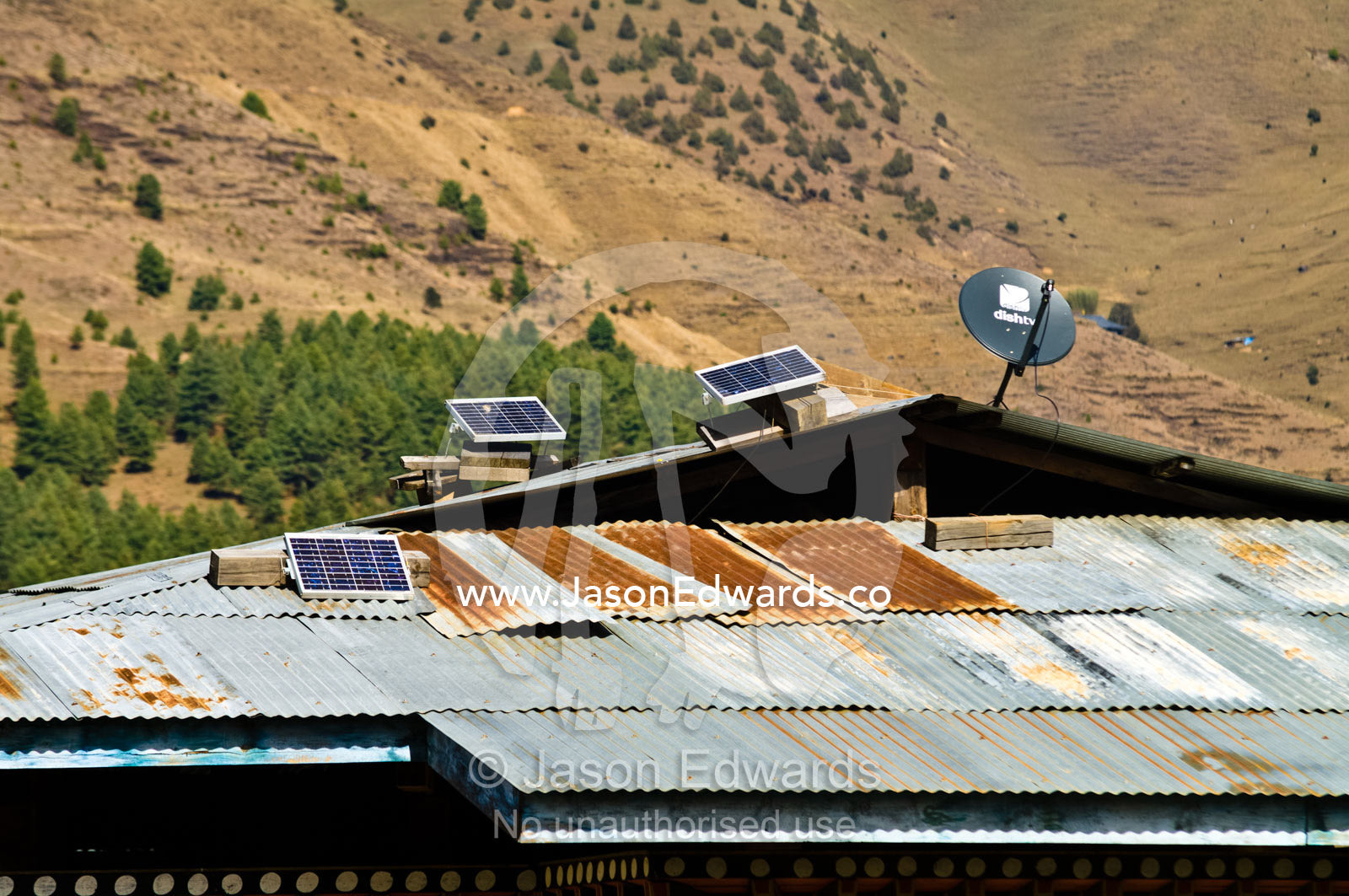 A solar panel generates electricity for a village home with a corrugated tin roof held in place by rocks. Ganteng, Wangdue Phodrang District, Phobjika Valley, Phobjikha Valley, Gangteng Valley, Black Mountains, Bhutan.