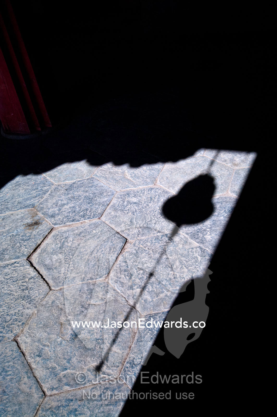 The shadow of a brass bell and chain hanging in a doorway to a Buddhist monastery. Gangteng Monastery, Ganteng, Wangdue Phodrang District, Phobjika Valley, Phobjikha Valley, Gangteng Valley, Black Mountains, Bhutan.