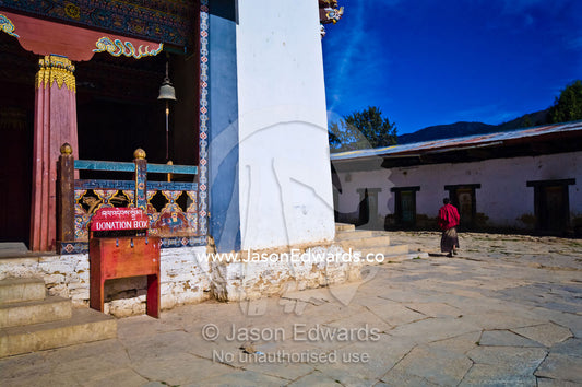 A Buddhist monk walking through the courtyard of an ancient monastery. Gangteng Monastery, Ganteng, Wangdue Phodrang District, Phobjika Valley, Phobjikha Valley, Gangteng Valley, Black Mountains, Bhutan.