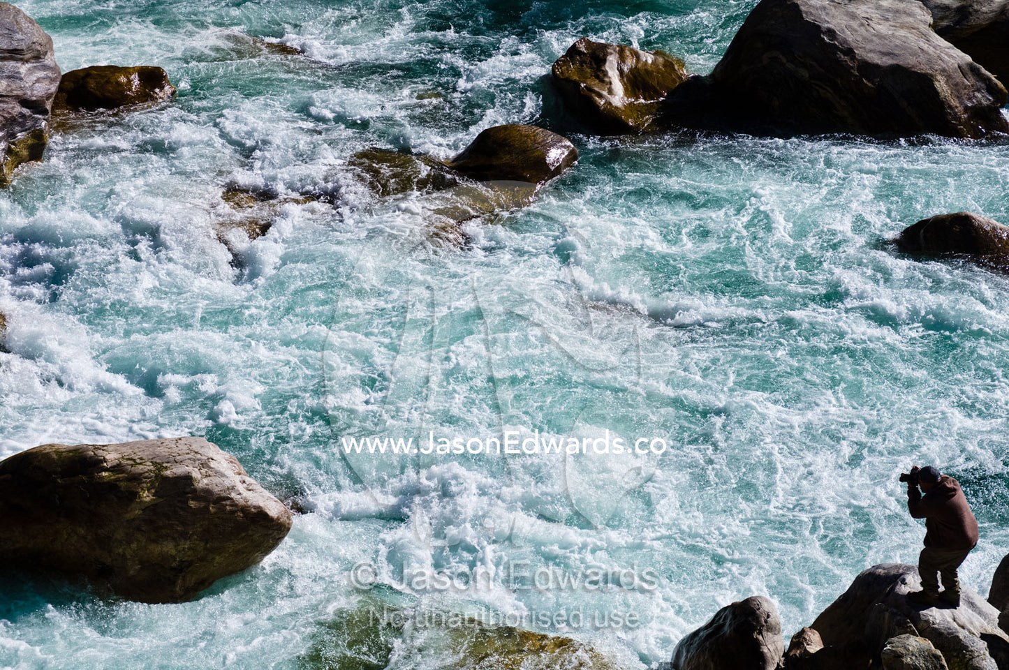 A photographer captures the swirling rapids of a pristine Himalaya river from a boulder on the shore. Punakha River, Punakha Valley, Punakha-Wangdiphodrang District, Bhutan.